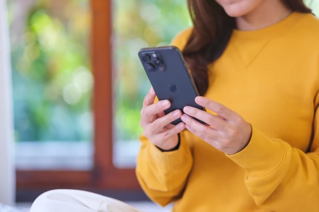 kobieta trzyma iphone na łóżku